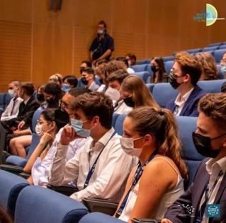 Jongeren met mondmaskers in een auditorium, kijkend naar de spreker links buiten beeld